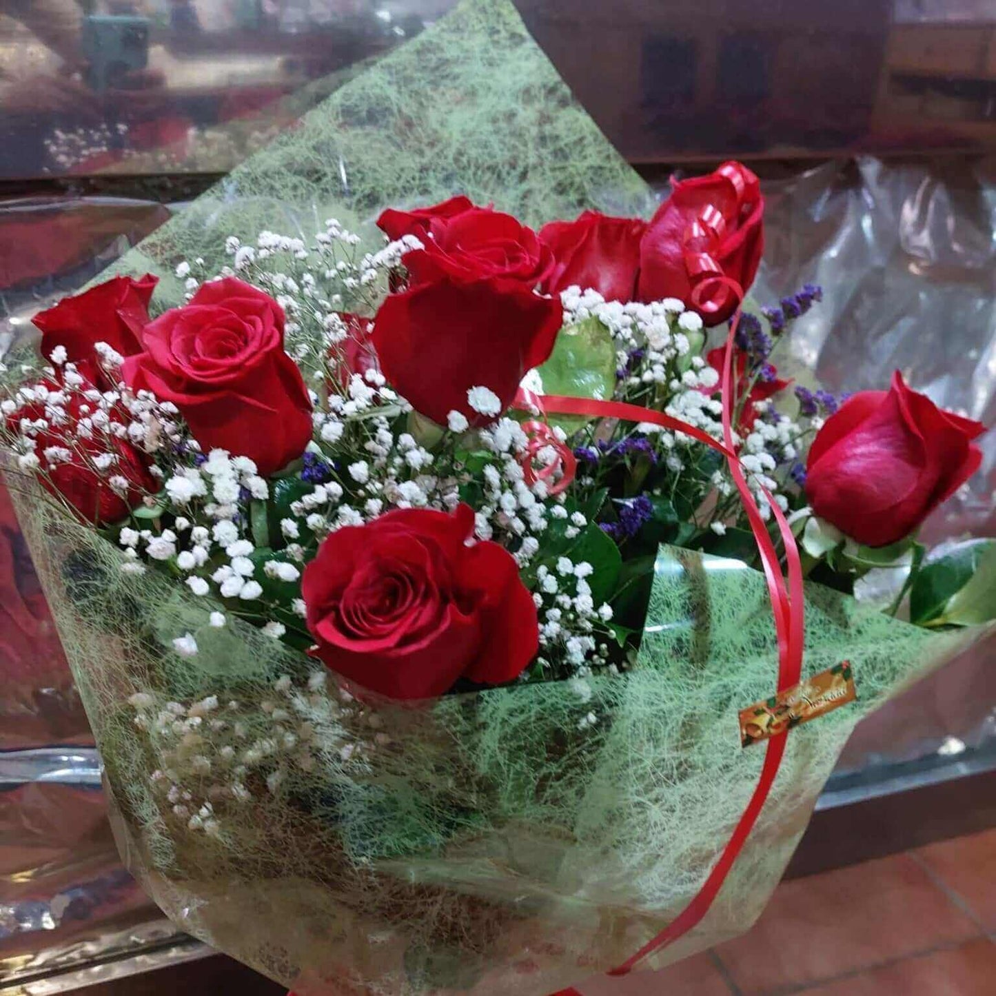 Ramo de rosas rojas con paniculata y flores verdes en un envoltorio, ideal para regalos.
